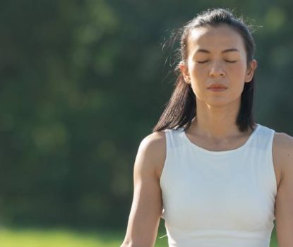 Woman on a yoga mat to relax in the park at mountain lake. Calm woman with closed eyes practicing yoga, sitting in Padmasana pose on mat, Lotus exercise, attractive sporty girl in sportswear.